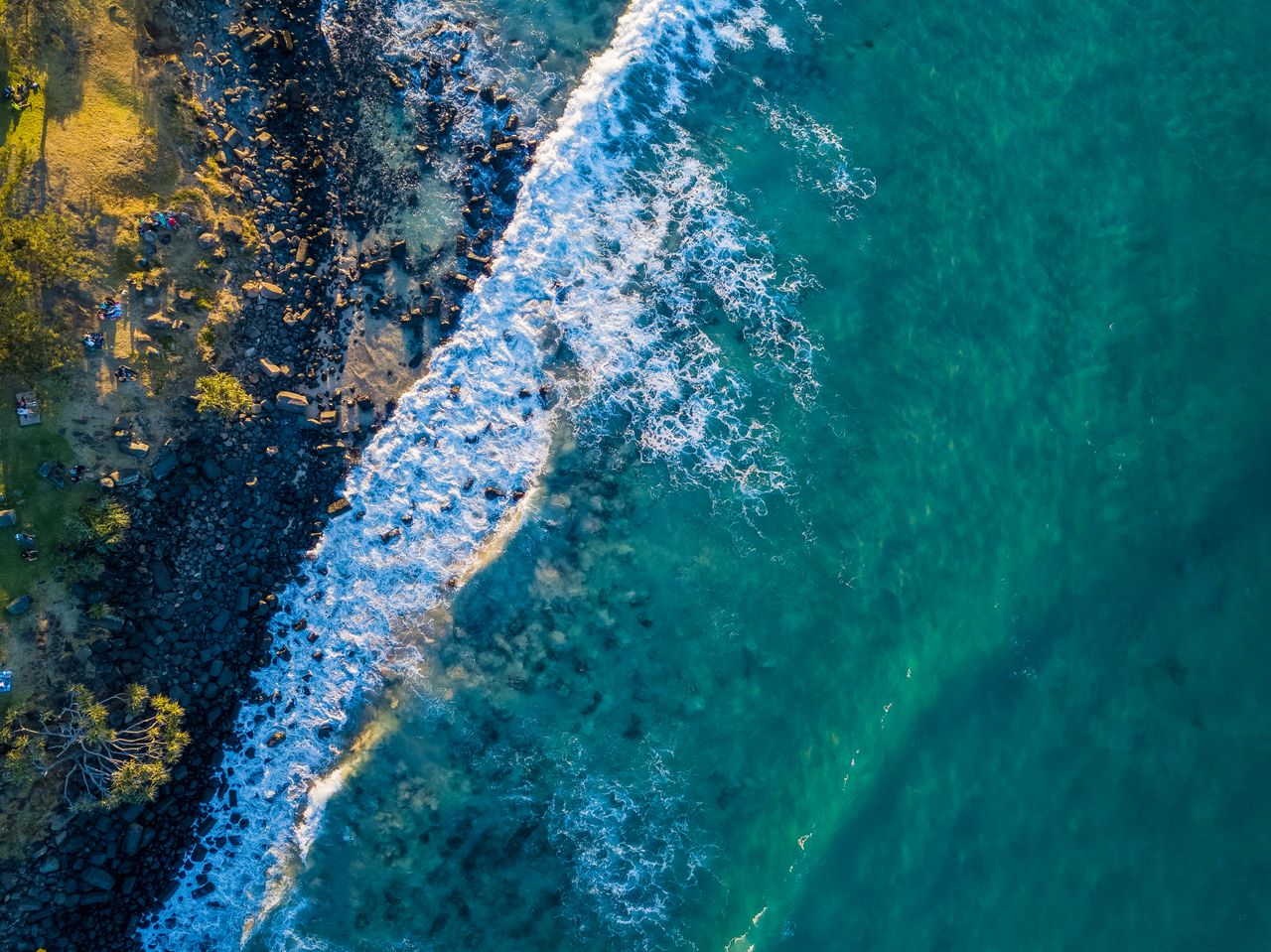 Home A breathtaking aerial view showcasing turquoise ocean waves crashing against a rocky shoreline.